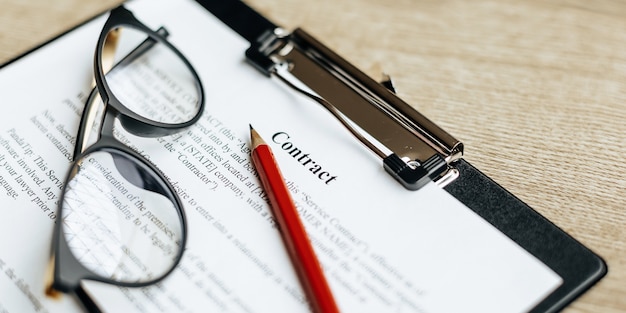 Foto een contract op een houten werktafel met een bril en een rood potlood. de documenten zijn klaar voor ondertekening. bedrijfsconcept. samenwerkingsovereenkomst.