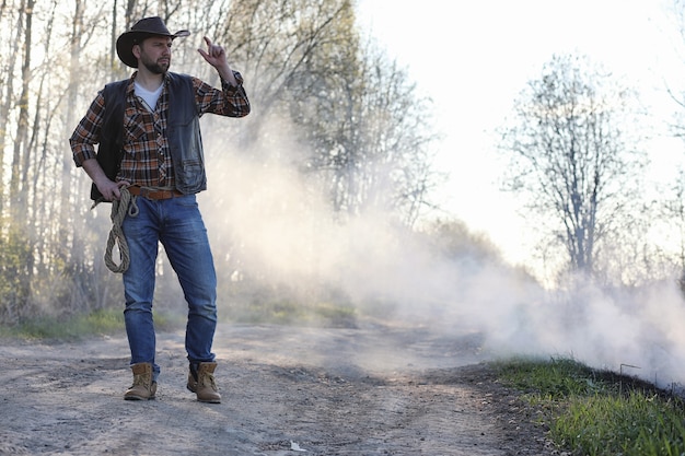 Een cowboy in een hoed en vest staat in een dikke rook op de weg