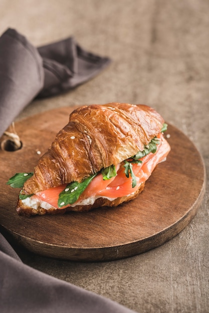Een croissantsandwich met zalm, ricotta en rucola op een houten bord met een servet