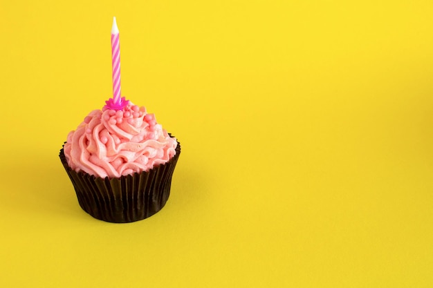 Een cupcake met roze room en kaars op de gele achtergrondkopieer de ruimte