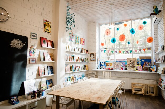 Een deel van het interieur van de klas met houten tafel in het midden, schoolbord op bakstenen muur en boeken op planken