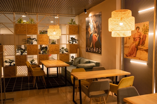 Een deel van het interieur van een gezellig modern café met houten tafels, fauteuils, huisplanten en posters op muren