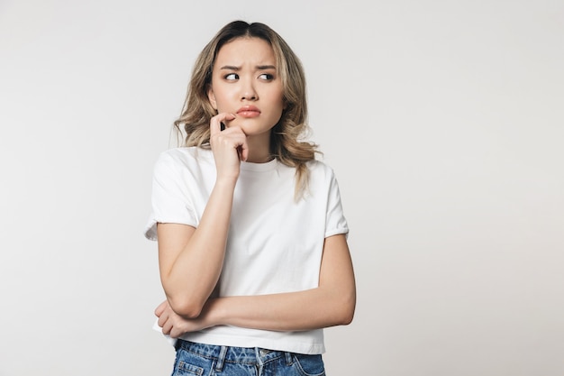 een denkende schattige jonge vrouw poseren geïsoleerd over een witte muur muur