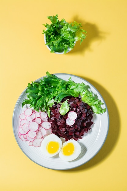 Een dieetgerecht gemaakt van groenten. Bietentartaar, radijs, friessalade en gekookt ei op een bord op een gele tafel. Boven- en verticaal aanzicht
