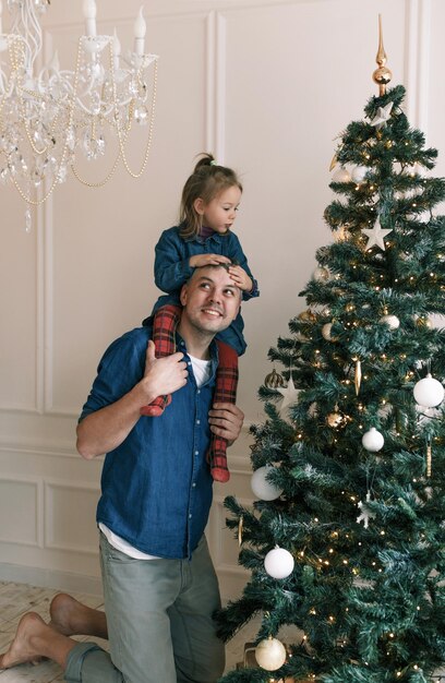 Een dochtertje speelt met haar vader zittend op zijn schouders terwijl ze een kerstboom versiert