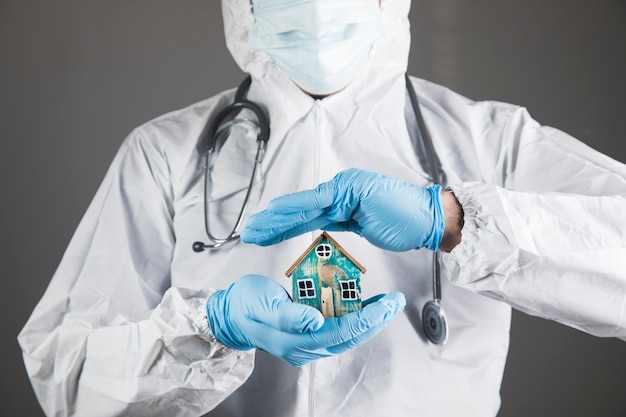 Een dokter in een wit beschermend uniform beschermt een klein huis op een grijs tafereel