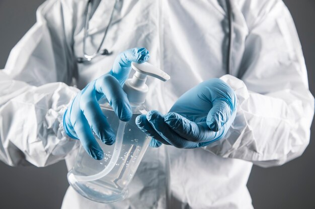 Een dokter in een wit beschermend uniform wast zijn handen met een ontsmettingsmiddel op een grijs tafereel