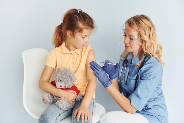 Een dokter in uniform die een teddybeer vasthoudt en de patiënt vaccinatie geeft.