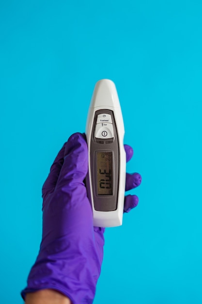 Een doktershand die een paarse handschoen draagt met een thermometer op een blauwe achtergrond