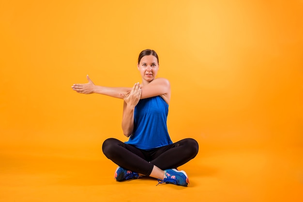 Een donkerbruine vrouw in een sportuniform doet een rekoefening op een oranje muur