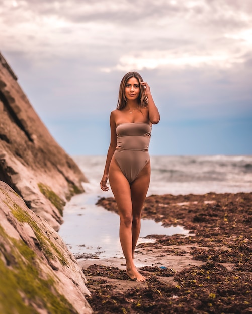 Een donkerharige blanke vrouw in een bruin zwembroek op een natuurlijke achtergrond aan zee