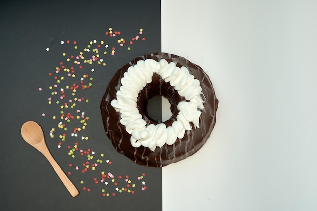 Een donut bedekt met chocolade met wit glazuur en een paar gekleurde hagelslag aan de linkerkant.