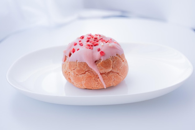 Een donut met roze glazuur en hagelslag bovenop zit op een bord.