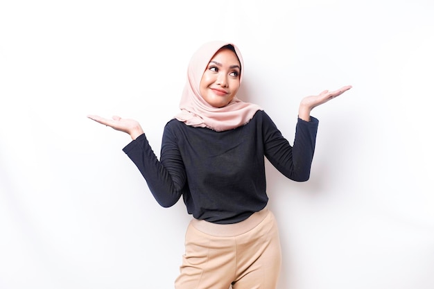 Een doordachte jonge Aziatische moslimvrouw draagt hijab en ziet er verward uit tussen keuzes geïsoleerd door een witte achtergrond
