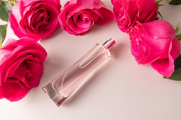 Een doorzichtig flesje damesparfum of eau de toilette ligt tussen de grote toppen van roze rozen Bovenaanzicht Sjabloon voor productpresentatie