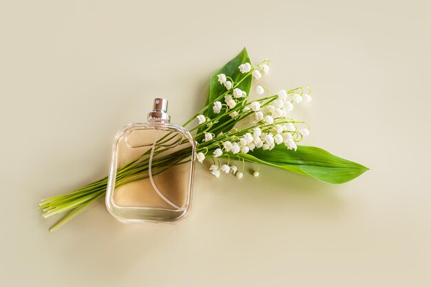 Een doorzichtige fles parfum met een delicaat aroma van lente lelies van de vallei ligt op een boeket bloemen Pastel achtergrond