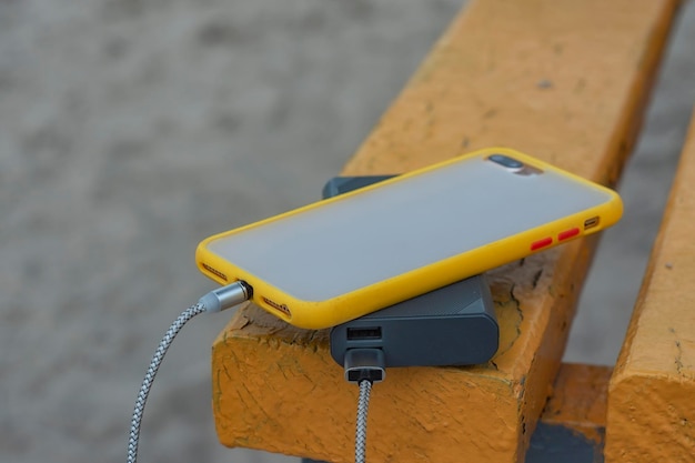 Een draagbare oplader laadt de smartphone Power Bank op met kabel tegen de achtergrond van een houten bank