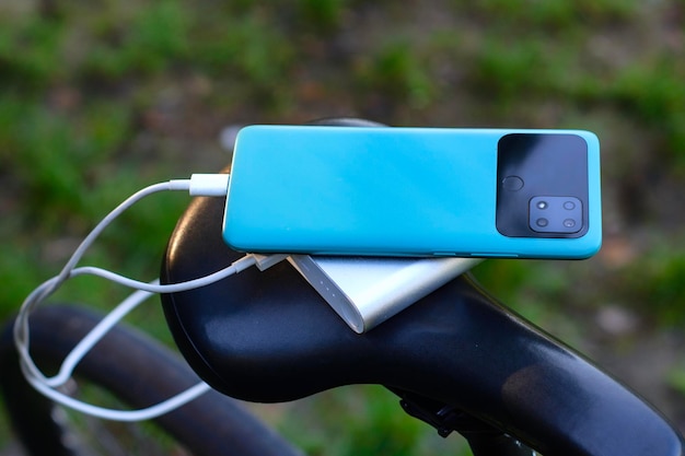 Een draagbare oplader laadt een smartphone op op de achtergrond van een fiets en natuur Power Bank op een reis om gadgets op te laden