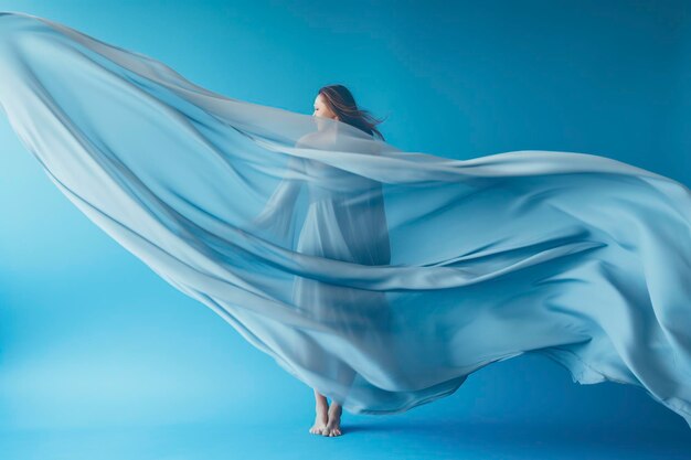 Een drijvende blauwachtige jurk gedragen door een slanke vrouw die op een eenvoudige minimalistische achtergrond danst