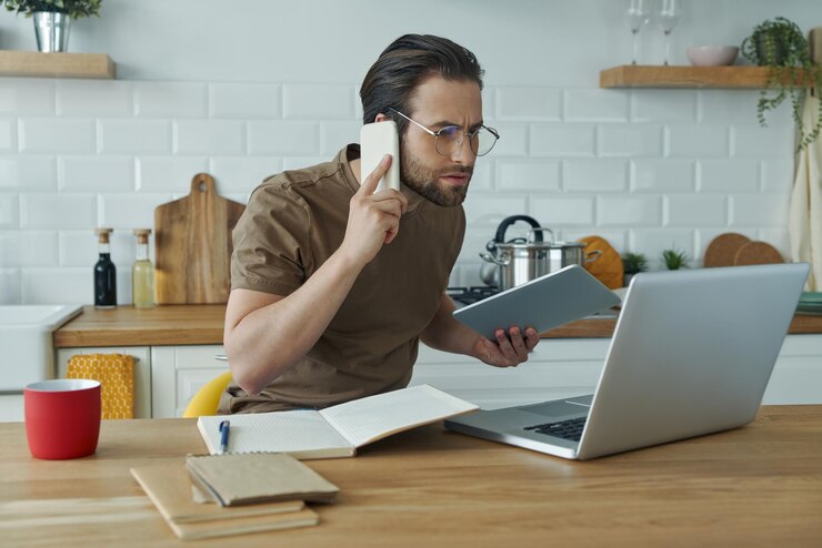 Foto een drukke jonge man die thuis aan het werk is en op zijn mobiele telefoon praat en technologieën gebruikt