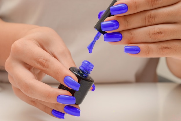Een druppel nagellak druipt van de rand van de borstel close-up vrouwelijke handen houden blauwe nagellak vast