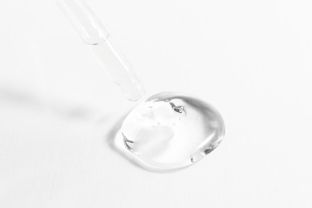 Een druppel transparante cosmetische gel op een witte achtergrond met een close-up van een glazen druppelaar