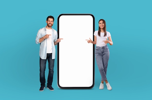 Een duizendjarige man en vrouw staan naast elkaar en wijzen vrolijk naar een reusachtig leeg smartphone-scherm