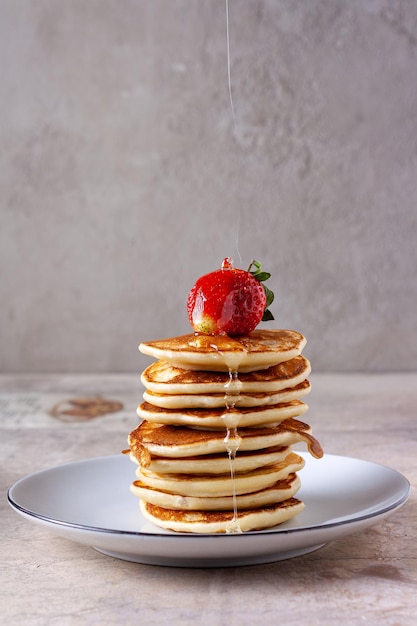 Een dun straaltje honing giet op aardbeien op een stapel pannenkoeken