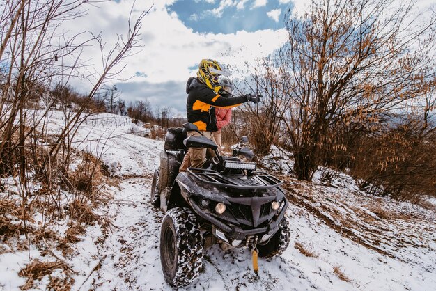Een echtpaar geniet van het rijden van een quad op de top van een berg in de winter