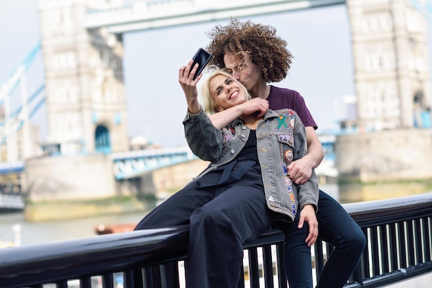Foto een echtpaar neemt een selfie terwijl ze tegen de torenbrug zitten.