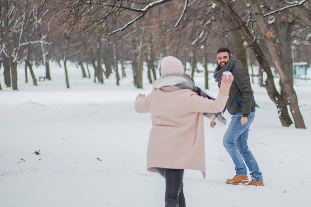 Een echtpaar speelt op sneeuw tegen kale bomen.