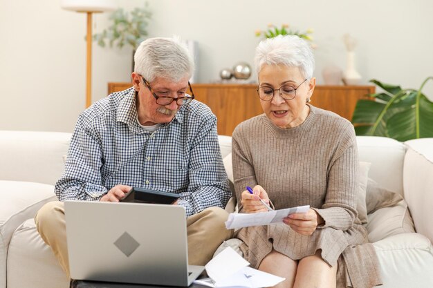 Foto een echtpaar van middelbare leeftijd zit met een laptop en een papieren document. een oudere volwassen man en vrouw lezen een krant.