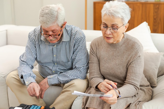 Foto een echtpaar van middelbare leeftijd zit met een laptop en een papieren document. een oudere volwassen man en vrouw lezen een krant.
