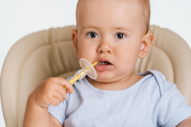 Een eenjarig kind zit op een stoel met een tandenborstel in zijn handen. Tanden poetsen door een pasgeboren baby