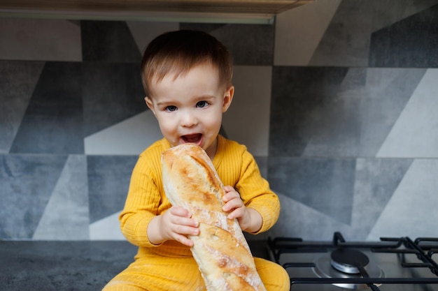 Een eenjarige kleine jongen in gele kleren zit en eet versgebakken roggebrood Het kind houdt een vers stokbrood in zijn handen
