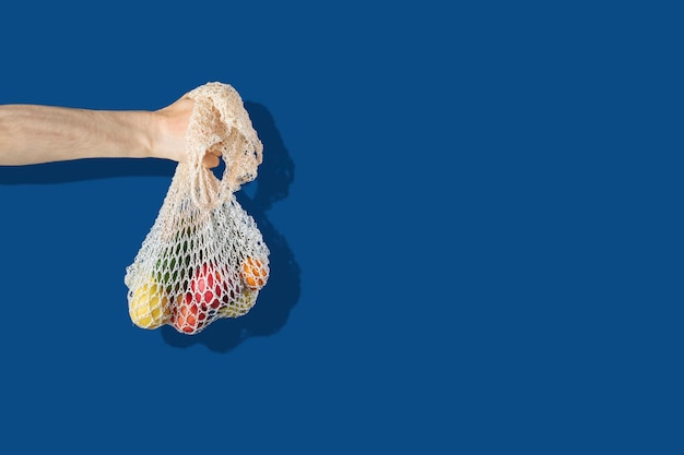 Foto een eenvoudig abstract beeld van de hand met een eco-tas van mesh-katoen tegen de kleurenmuur, recyclen zonder afval