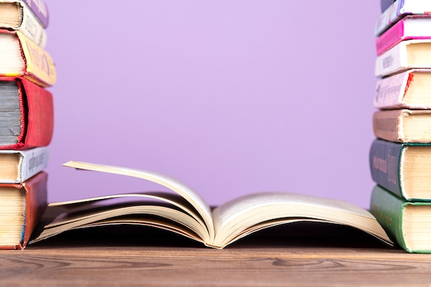 Een eenvoudige compositie van veel hardback-boeken, veelkleurige boeken op een houten tafel en een lila gekleurde achtergrond.