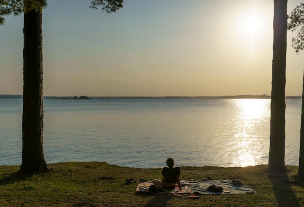 Een eenzaam meisje rust en bewondert de zonsondergang aan de oever van een bosmeer Ontspannen levensstijl