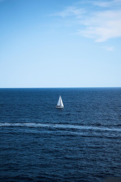 een eenzame witte zeilboot omringd door diepblauw water en een heldere blauwe lucht