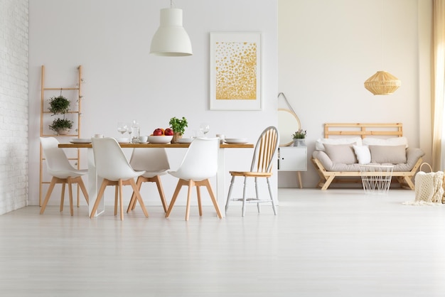 Een eetkamer met een witte muur en een houten tafel met witte stoelen en een witte bank.