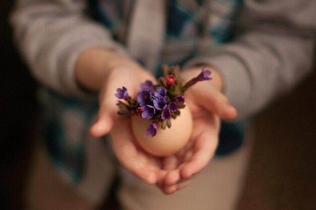 Een ei met bloemen in de handen van een kind met een wazige achtergrond