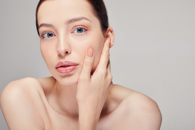 Een elegant verfijnd mooi meisje met volle lippen, donker haar en stralende schone delicate huid op de. Dame kijkt loom recht met open mond en hand vasthouden