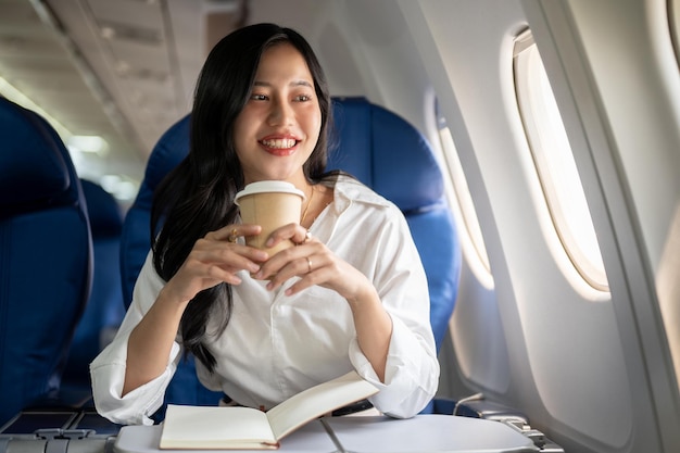 Een elegante Aziatische zakenvrouw drinkt koffie terwijl ze naar het uitzicht buiten het vliegtuigraam kijkt