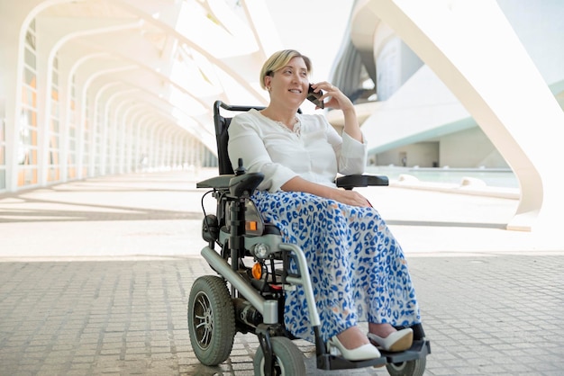 Een elegante en glimlachende vrouw met een handicap die in een rolstoel zit te praten op een mobiele telefoon