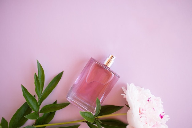 Een elegante fles damesparfum of toiletwater op een roze achtergrond met bladeren en een pioenroos bovenaanzicht een kopie van de ruimte