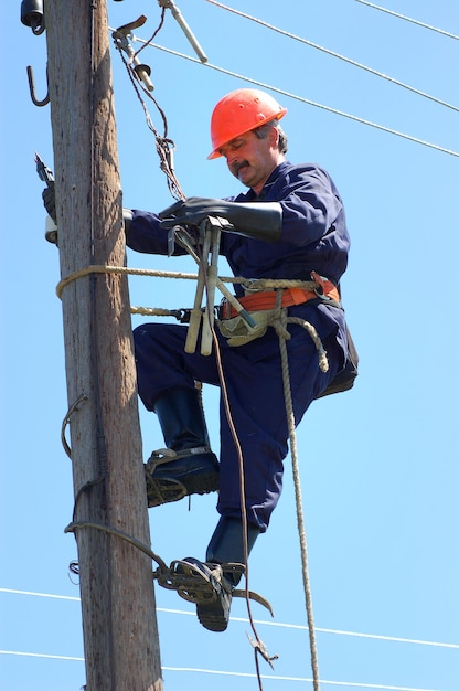 Een elektricien klimt op een houten steun om een hoogspanningsleiding te repareren