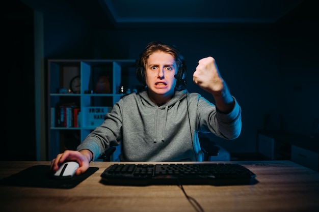 Een emotionele gamer-streamer in een headset zit thuis achter de computer en kijkt boos naar de camera