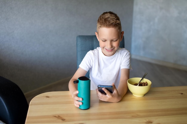 Een emotionele jongen in een wit T-shirt verbindt de luidspreker met de telefoon en lacht