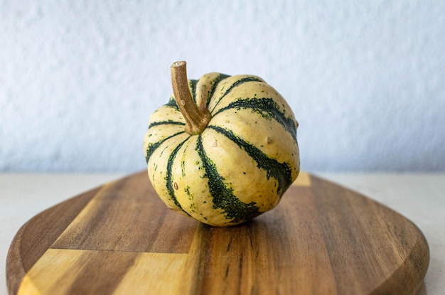 Een enkele mini groene en witte decoratieve pompoen op een houten snijplank