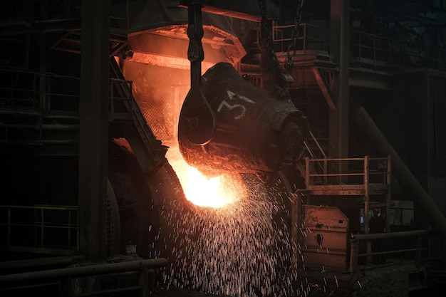 Een enorme pollepel giet roodgloeiend ijzer in een oven in een fabriek waaruit vonken vliegen